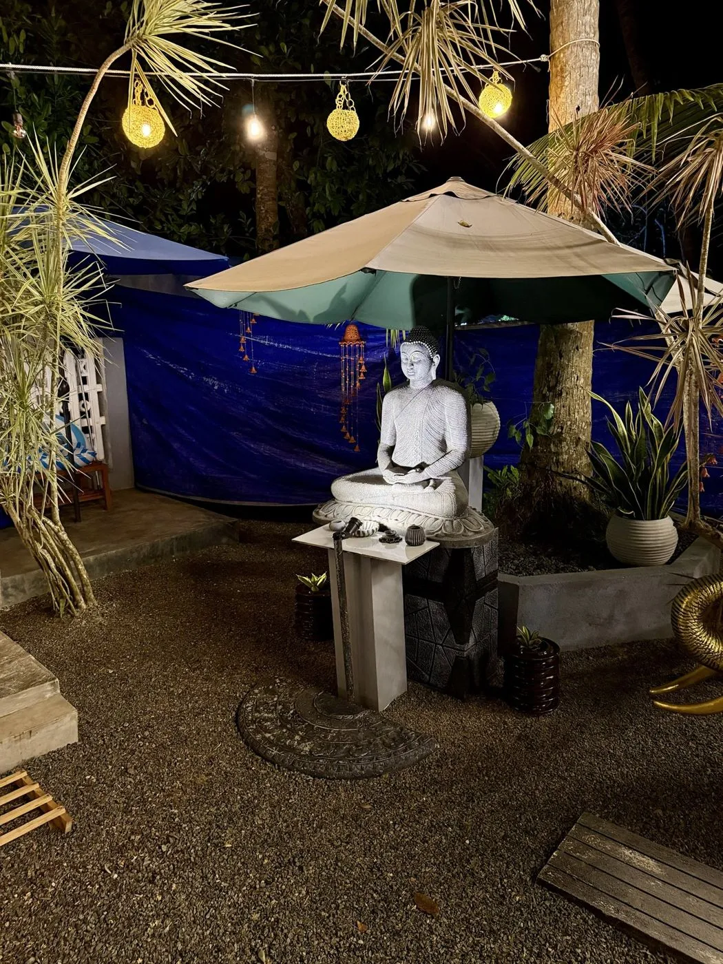 A seated Buddha under a garden umbrella, with a moonstone at its feet