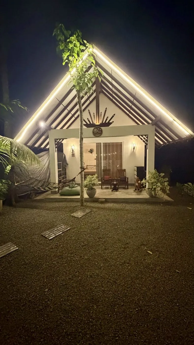 My cottage at night: the A-frame roof outlined in light, hammock and bean bag on the porch