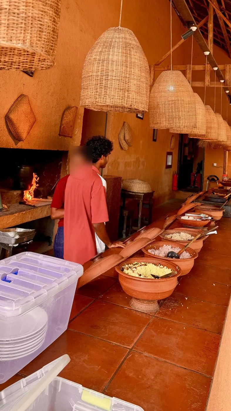 Clay-pot buffet line under wicker lamps, wood fire on the left