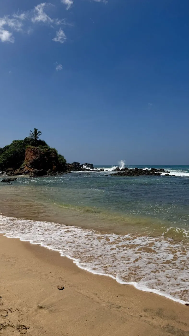 Parrot Rock, Mirissa: a red-earth outcrop with one palm, waves bursting on the rocks