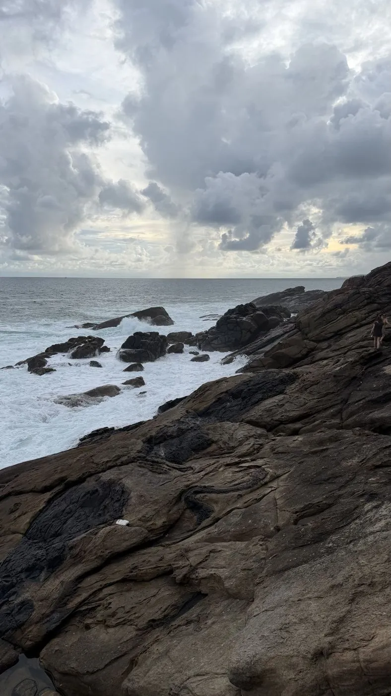 Out on the rock ledge, surf breaking below and rain clouds rolling in